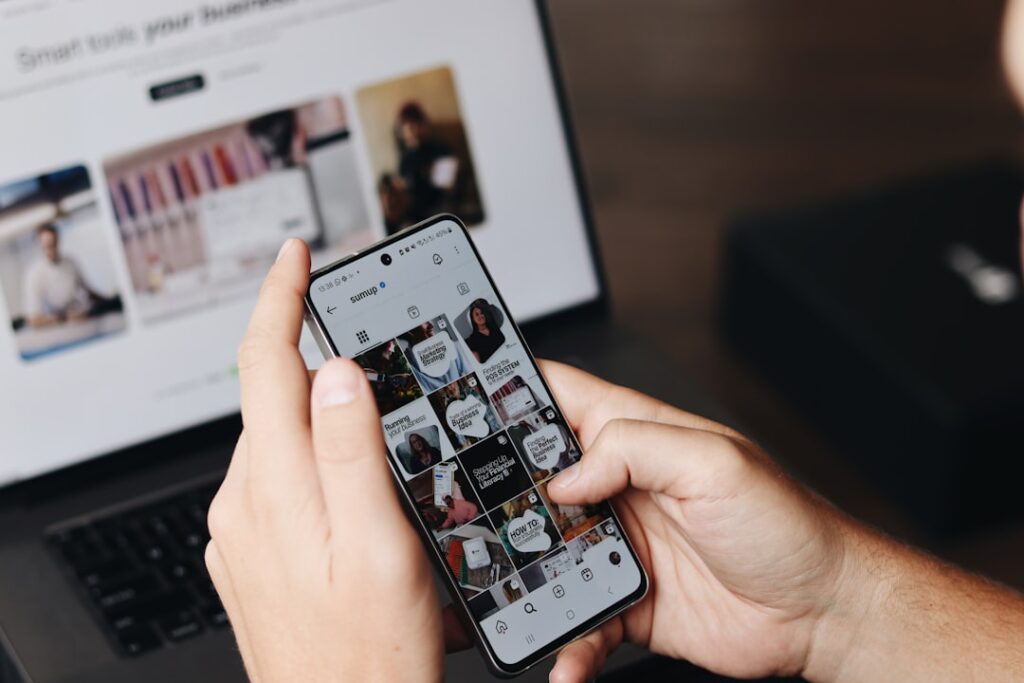 content marketing tips - A person is using their smartphone to browse the SumUp Instagram profile, focusing on posts related to marketing strategies and business tips. In the background, a laptop displays a webpage about tools for business growth, suggesting a workspace or content creation environment. This image highlights the use of social media for brand promotion, digital marketing, and business engagement, making it relevant for content creators, marketers, and entrepreneurs.